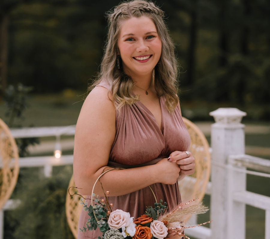 Ashley Daney smiling for the camera with a ring of flowers on her arm.