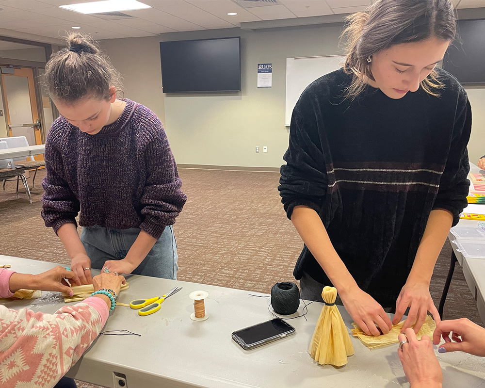 Sophomores, Brenna Smith, psychology major (left) and Shelby Zink, biology major, make traditional corn husk dolls