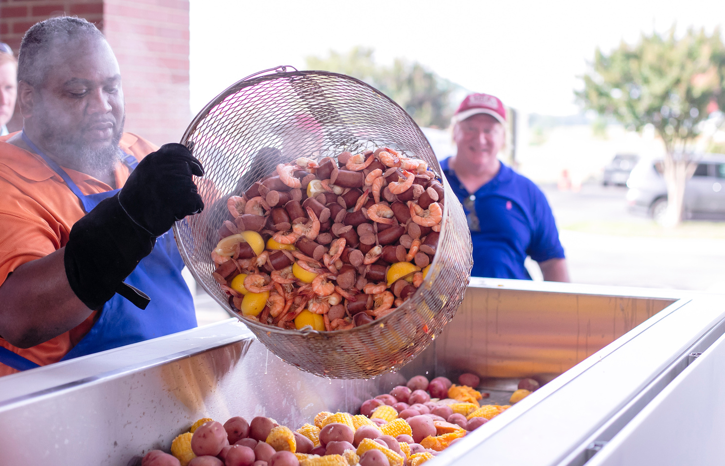 A man pours shrimp, sausage and potatoes into a long table for serving