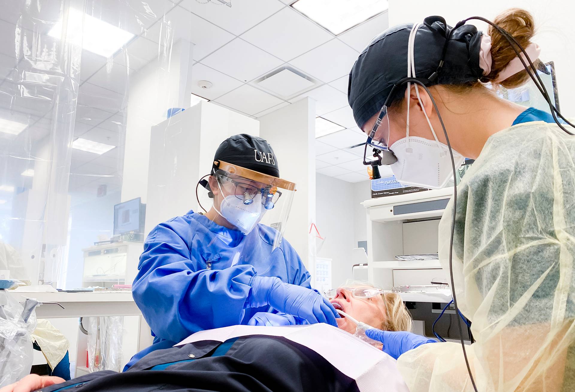 Emily Nguyen, left, and Isabel Jamison, senior dental hygiene major, clean a faculty volunteer's teeth at the UAFS Dental Hygiene Clinic, Wednesday, February 9, 2022.