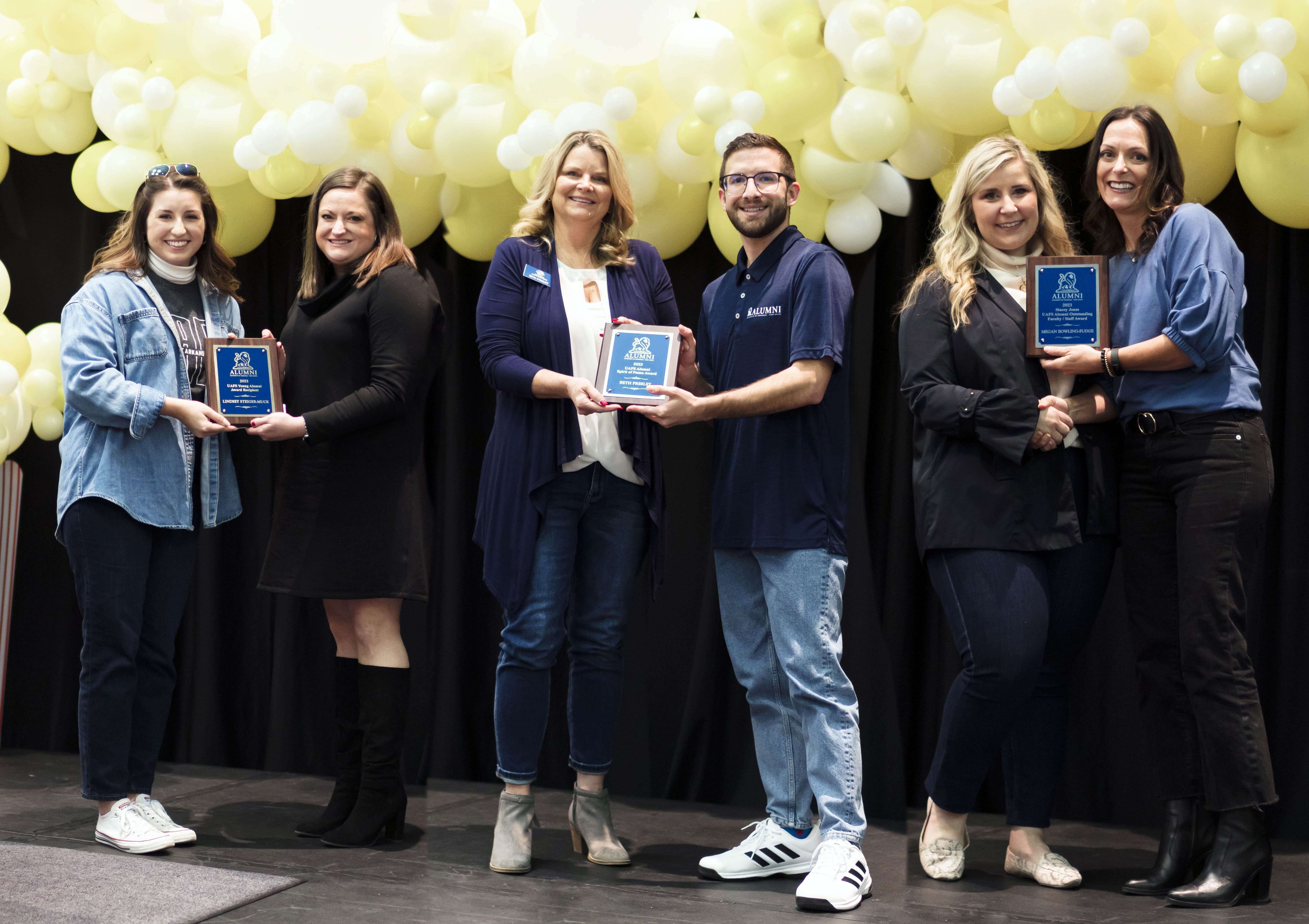 award winners stand on a stage with balloons behind