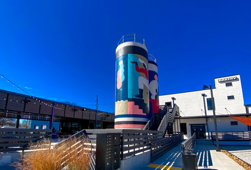 A painted silo stands infant of a white brick building.