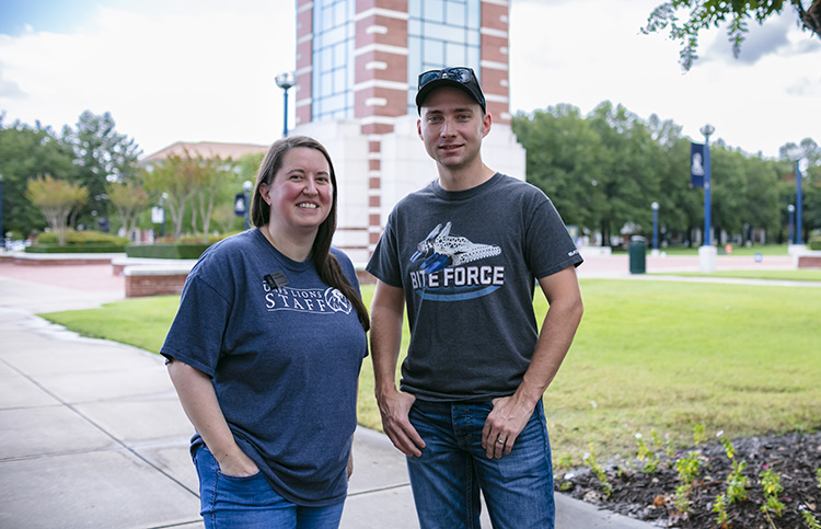 Two college siblings stand in front of university bell tower.