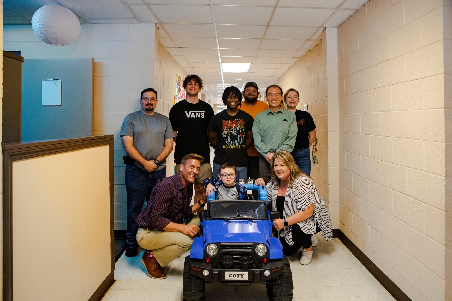 Students and professor pose with child, parents, and modified kiddie car