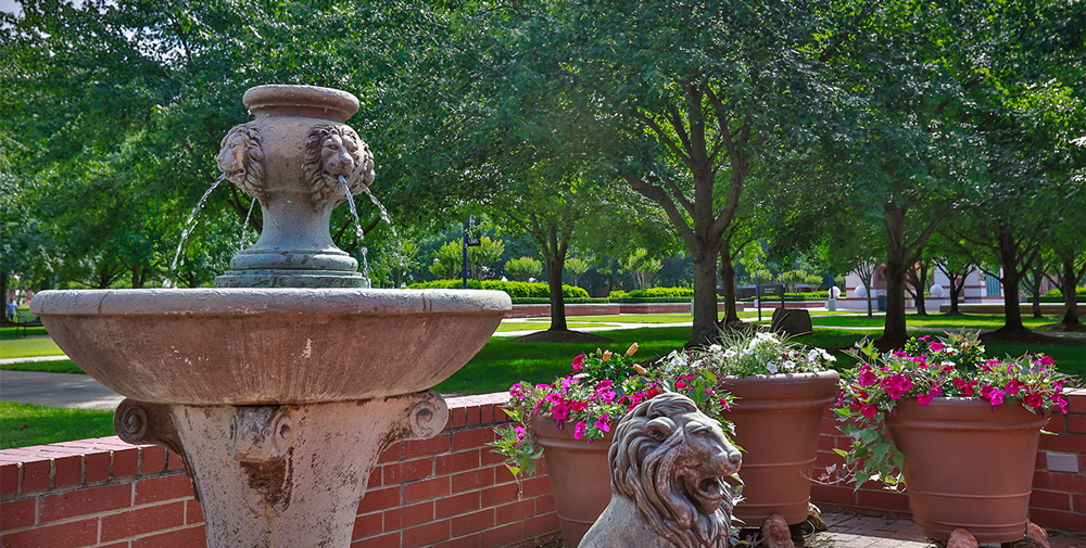 A view of the UAFS Campus Green from outside of Chancellor Riley's office with a lion fountain in the foreground.